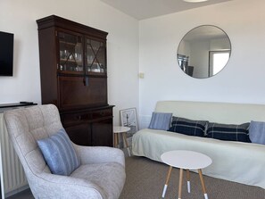 Un salon comprenant un canapé, un fauteuil, une petite table ronde et un meuble en bois.