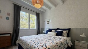 A bedroom with a bed, a window, a bedside table, and a hanging light fixture. - Comfortable family apartment - 4 guests (Saint-Pierre-d'Oléron)