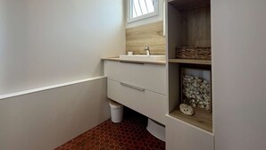 A bathroom with a white vanity, a mirror, a window, and a shelf with decorative items. - Comfortable family apartment - 4 guests (Saint-Pierre-d'Oléron)