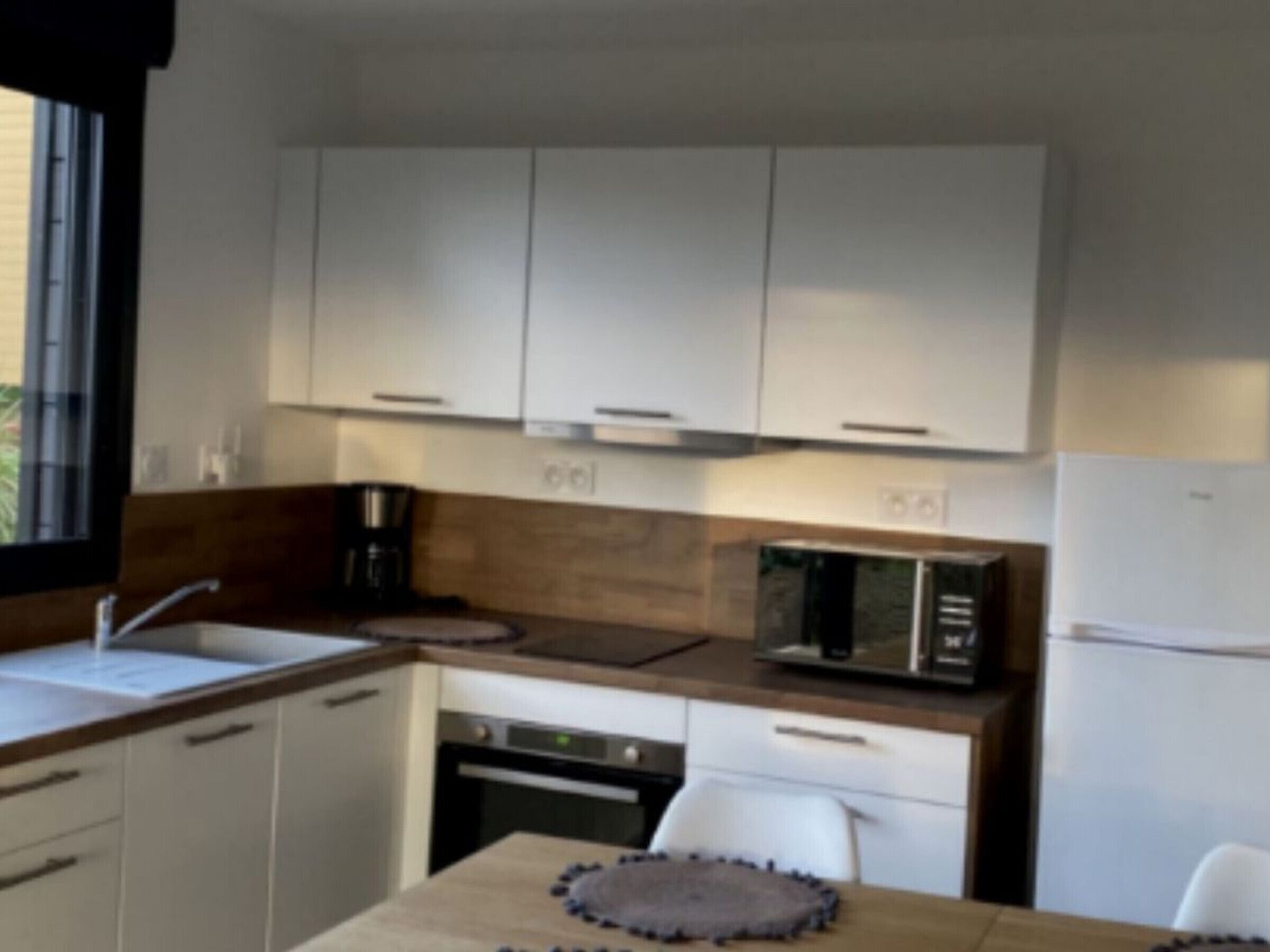 Une cuisine moderne avec des meubles blancs, un four à micro-ondes, une machine à café et un réfrigérateur.