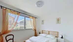 Ein Schlafzimmer mit einem Bett, einem Sessel, einem Nachttisch, einer Lampe und zwei gerahmten Bildern an der Wand.