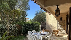 An outdoor patio with a stone floor, white plastic chairs, a table set for dining, and a pergola with a lantern. - Spacious apartment, calm and greenery - 7 guests (Saint-Raphaël)