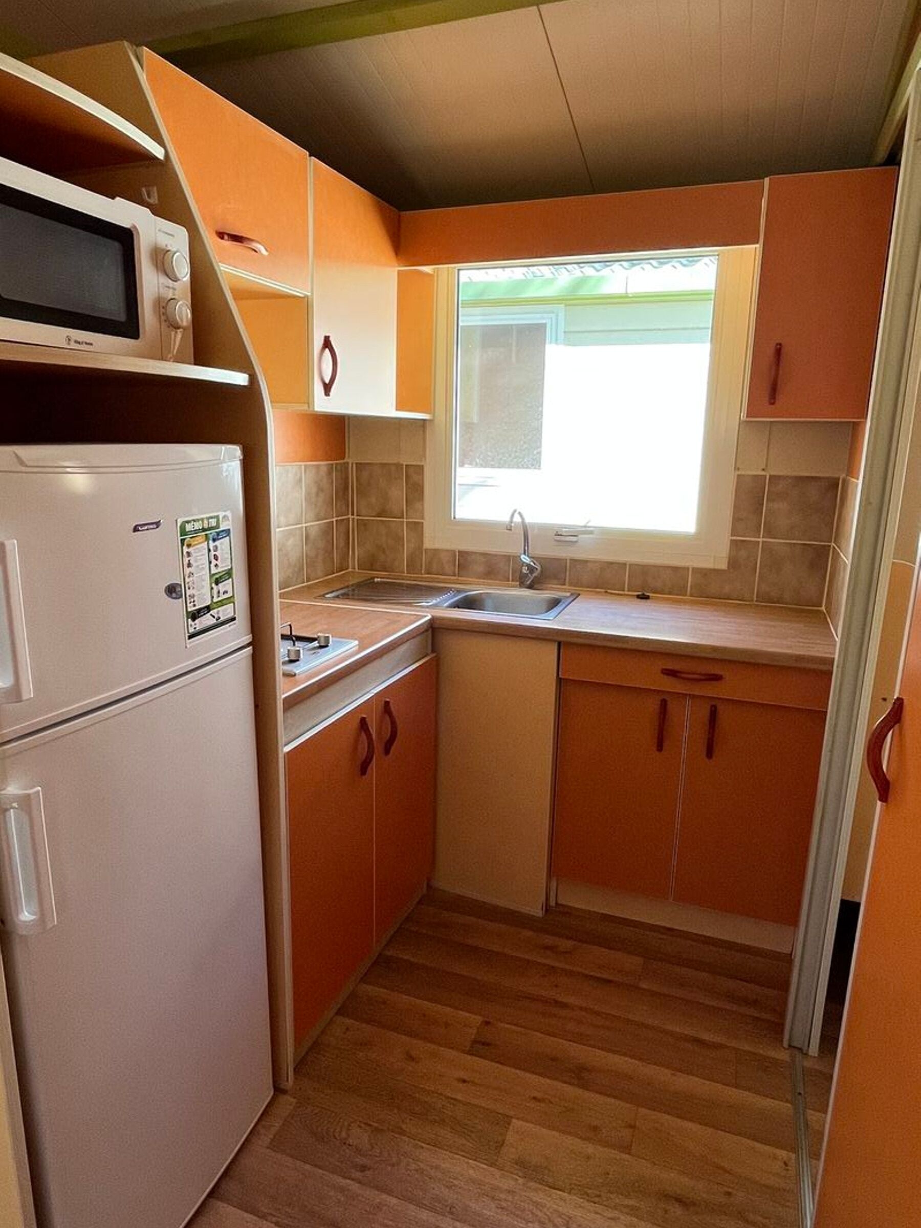Een functionele keuken met een koelkast, magnetron, spoelbak en houten kastjes.