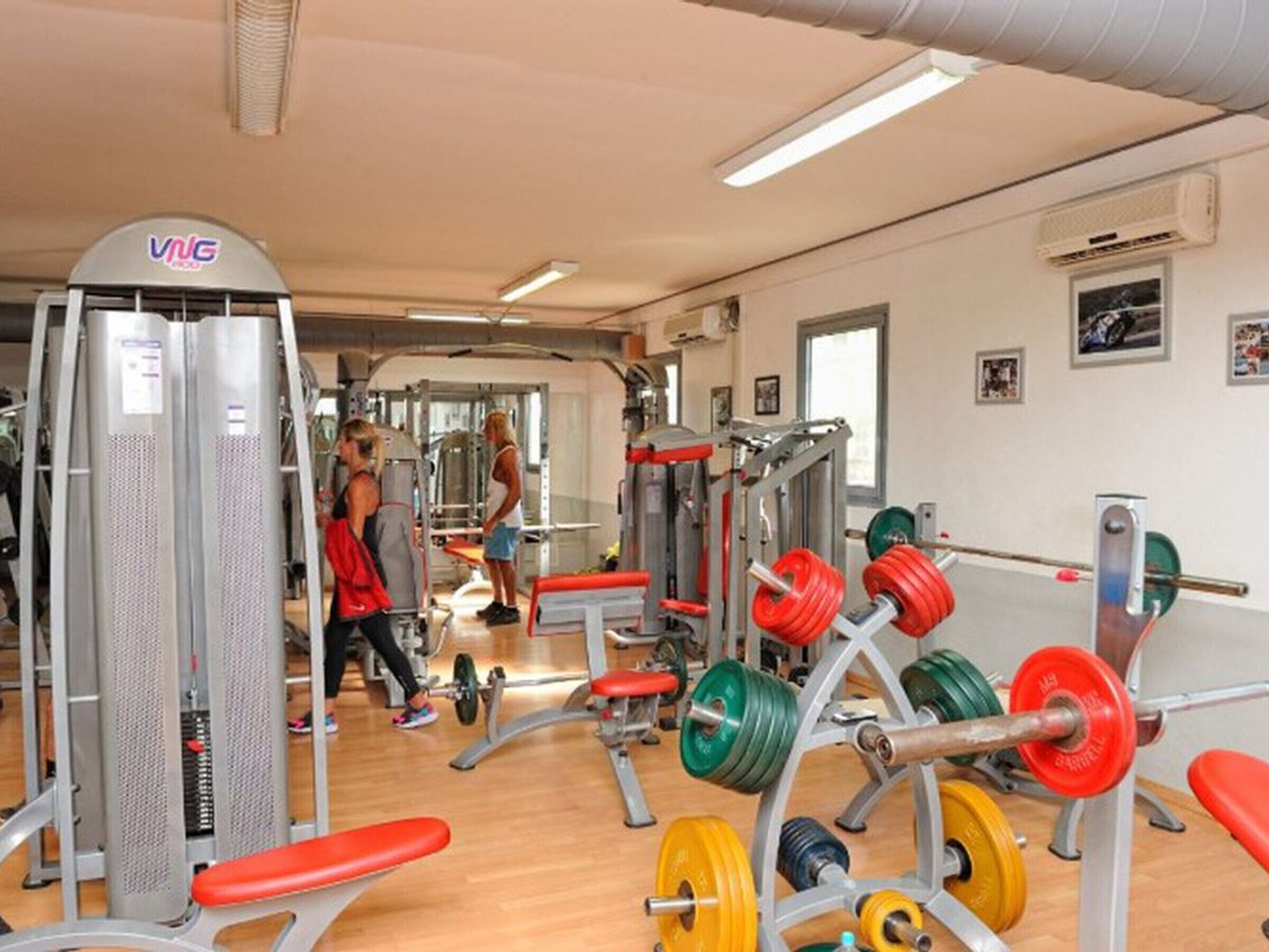 Un gimnasio con equipo de levantamiento de pesas, bancos y el logotipo de VNG en la pared.