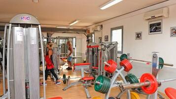 Un gimnasio con equipo de levantamiento de pesas, bancos y el logotipo de VNG en la pared.