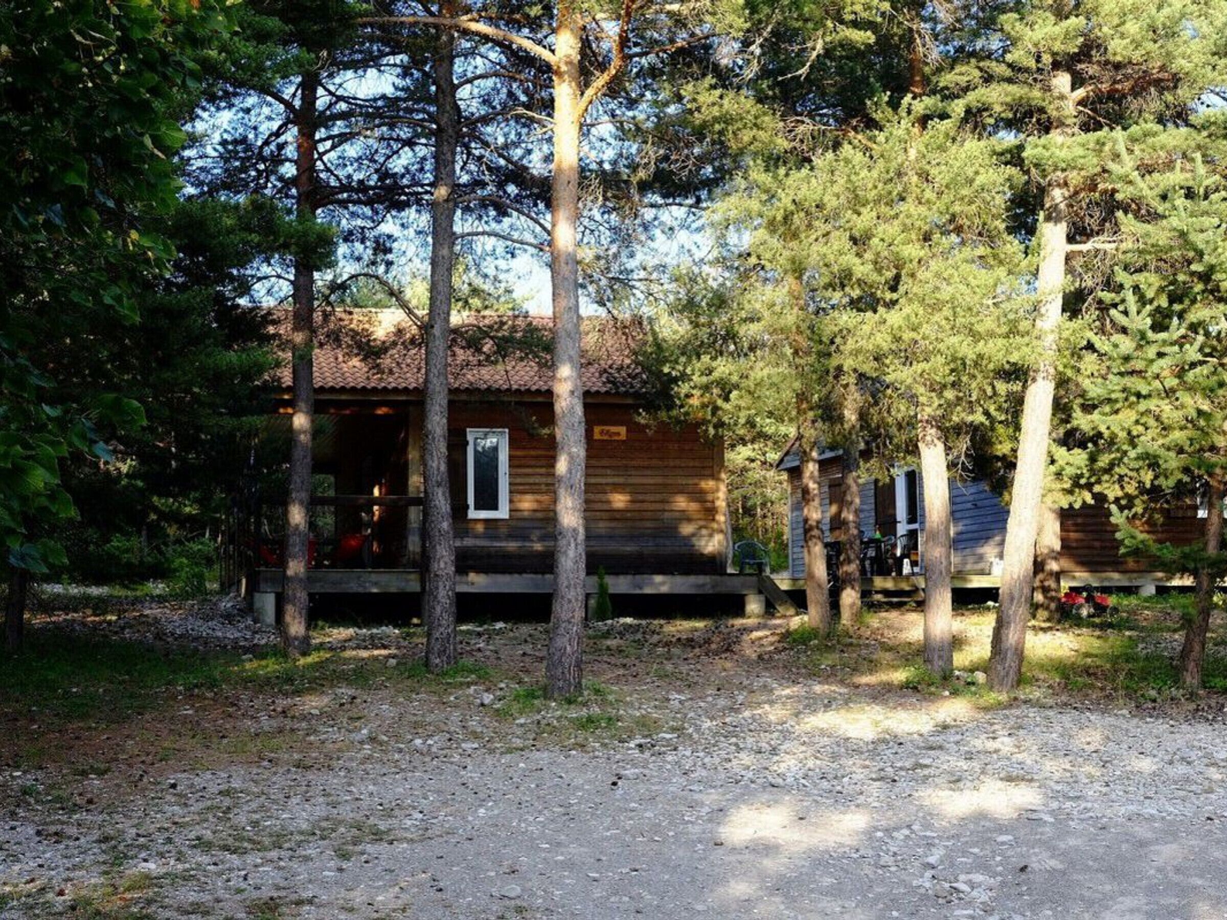 En rustik hytte med træfacade, veranda og grusgrund.