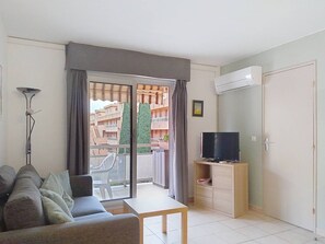 Ein Wohnzimmer mit einer Couch, einem Tisch, einem Fernseher, einer Stehlampe und einer Glastür, die auf einen Balkon im Freien führt.
