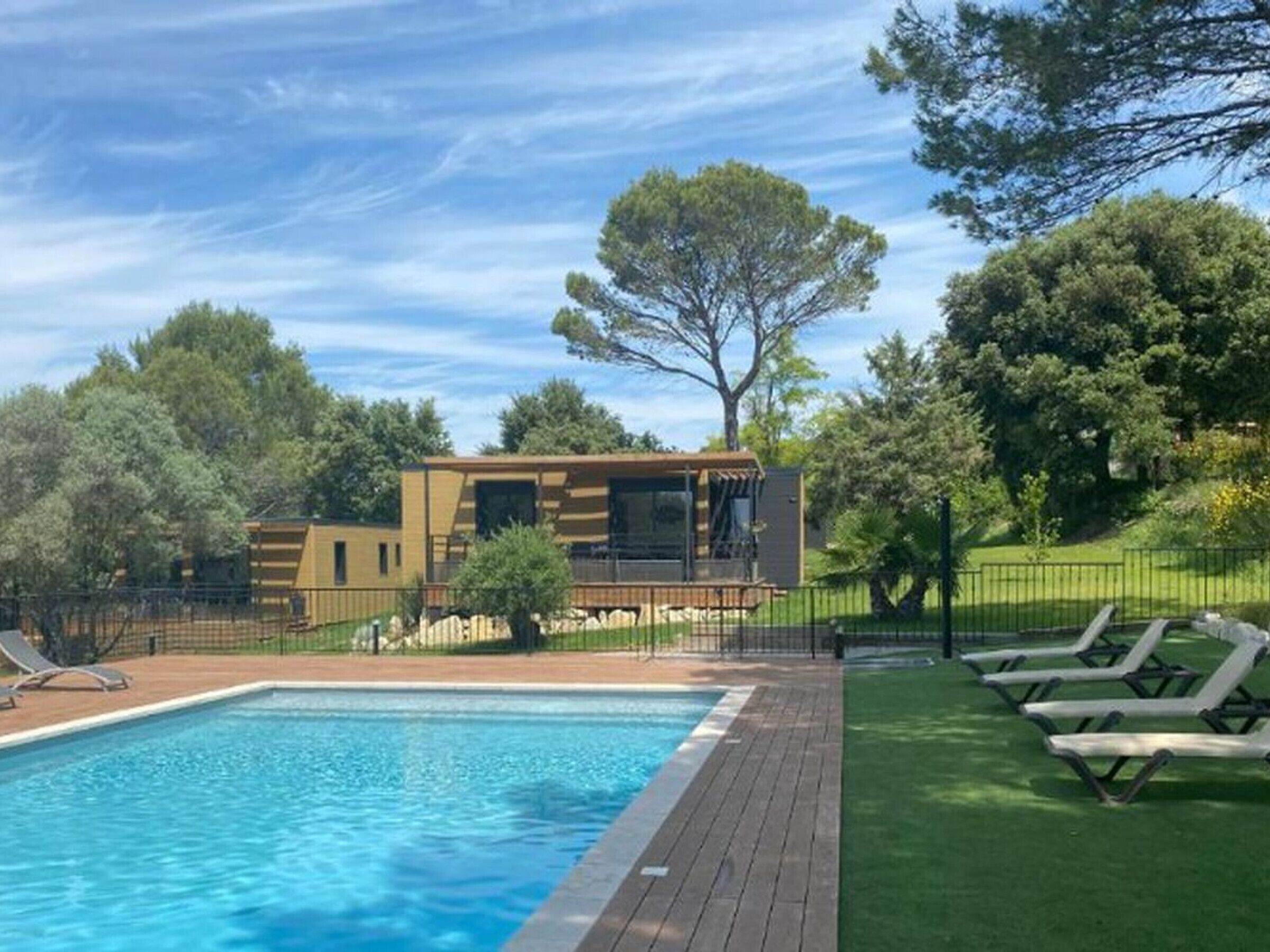 A pool area with a modern building, a fenced deck, and lounge chairs.
