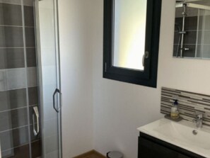 Ein Badezimmer mit Duschkabine aus Glas, einem weißen Waschbecken mit modernem Design und einem Spiegel darüber.