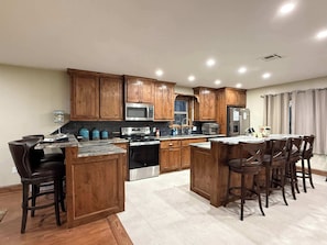 A modern kitchen with wooden cabinets, stainless steel appliances, and a central island with bar stools. - The Whole Zen Lodge: Main House+2 Private Hot Tubs (Lawton)