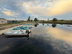 A calm body of water with boats docked on the left, a grassy area with trees, and a building on the left side. - The Whole Zen Lodge: Main House+2 Private Hot Tubs (Lawton)