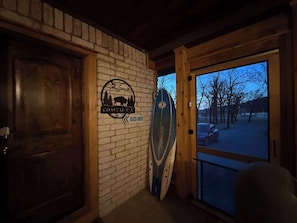 A wooden door, a brick wall with a logo, and a surfboard leaning against the wall. - The Whole Zen Lodge: Main House+2 Private Hot Tubs (Lawton)