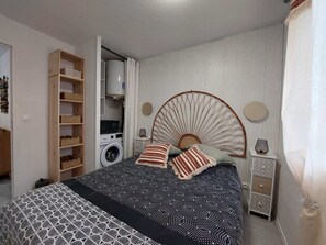 Ein Schlafzimmer mit Bett, Waschmaschine, Kleiderschrank und einem kleinen Tisch mit Lampe.