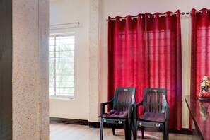 A room with a window, red curtains, two chairs, and a statue on a table.