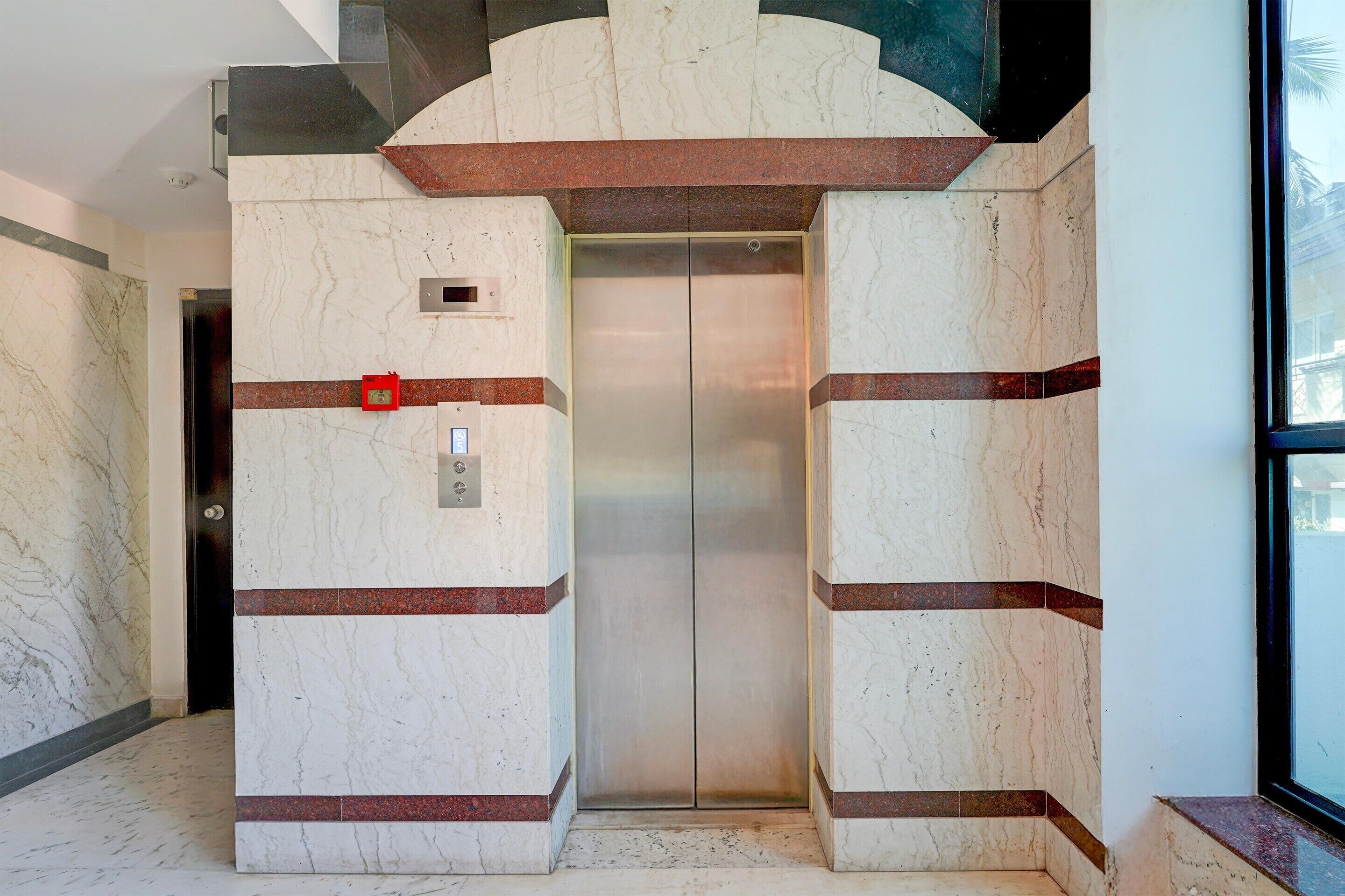 An elevator with marble walls and red accents, a door with a red lock, and a control panel.