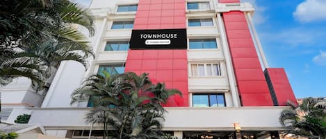 A multi-story building with a prominent red and white facade, a sign reading 'TOWNHOUSE,' and a well-maintained entrance area with steps leading to the door.
