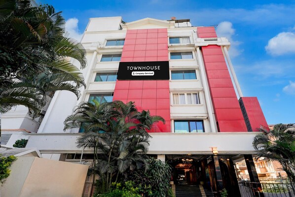 Un edificio de varios pisos con una fachada destacada en rojo y blanco, un letrero que dice 'TOWNHOUSE' y un área de entrada bien cuidada con escalones que conducen a la puerta.