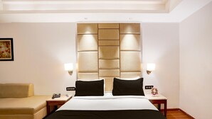 Een hotelkamer met een groot bed, een bank, een nachtkastje met een lamp en een kunstwerk aan de muur.