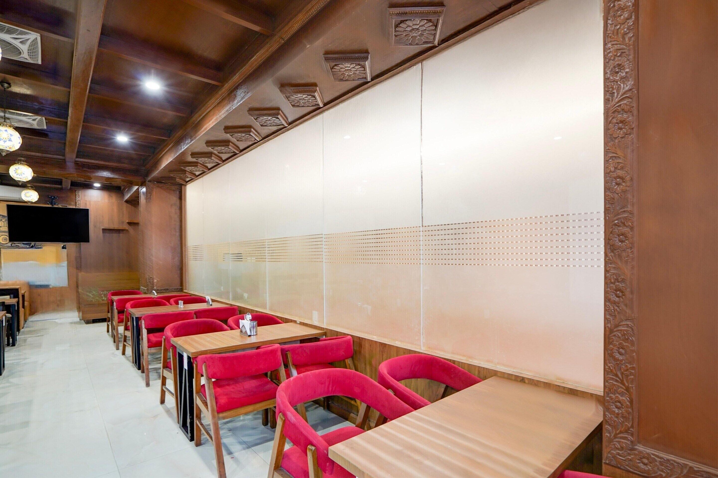Ein Restaurant mit Holztischen und roten Stühlen, einer weißen Trennwand und einem an der Wand befestigten Fernseher.