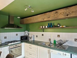 A kitchen with a gas stove, microwave, coffee maker, and a wooden ceiling beam. - Family farm cottage in the heart of nature, with jacuzzi & view of the horses (Thiembronne)