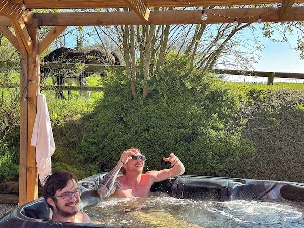 A hot tub with a wooden pergola overhead, surrounded by greenery and a fence. - Family farm cottage in the heart of nature, with jacuzzi & view of the horses (Thiembronne)