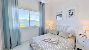 A bedroom with a bed, two bedside tables, a window with curtains, and two wall-mounted pictures.