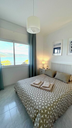 Un dormitorio con cama, mesita de noche, lámpara, ventana con vistas y radiador.