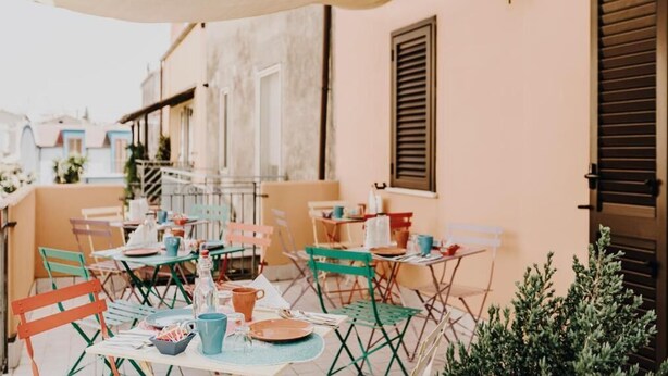 Un café al aire libre con mesas y sillas, un edificio con persianas y un farol.