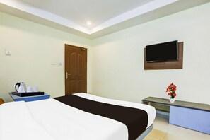 A hotel room with a bed, a TV mounted on the wall, a desk with a vase of flowers, and a coffee station. - Deluxe Hotel Rama Royal (Nellore)