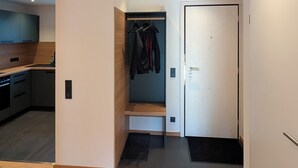 Interior moderno com chão de madeira, área de cozinha, corredor com cabides e uma porta.