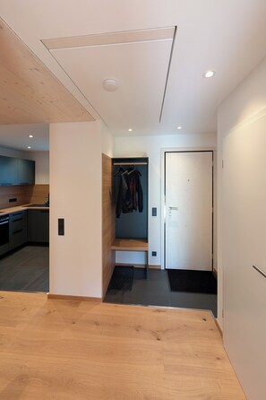 Un interior moderno con suelo de madera, una zona de cocina, un pasillo con perchero y una puerta.