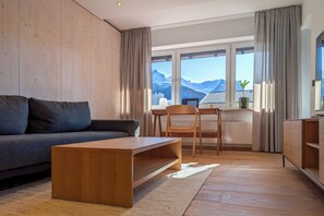 Una sala de estar moderna con sofá, mesa de centro de madera y vistas a montañas a través de grandes ventanales.
