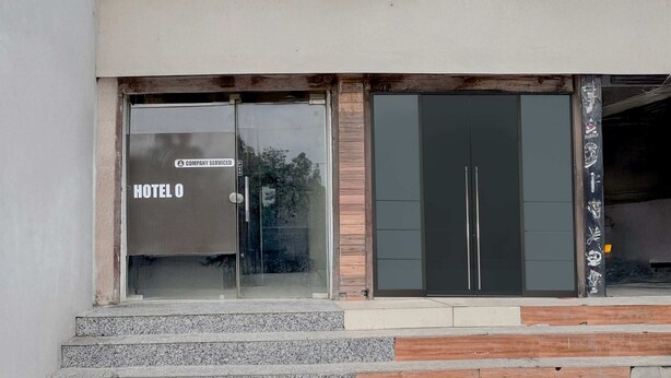 Entrada de hotel con puerta de vidrio que lleva la etiqueta 'HOTEL O' y un cartel que indica 'SERVICIO DE LA EMPRESA'.