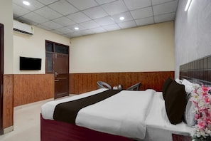 A hotel room with a bed, a television, a wooden wardrobe, and a window.