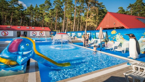 A swimming pool with a water slide, lounge chairs, and a building with a red roof. - Two-story Holiday Home Right on the Beach, Pool (Leba)