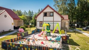 A residential area with a house, a playground, and a fenced play area with children. - Two-story Holiday Home Right on the Beach, Pool (Leba)