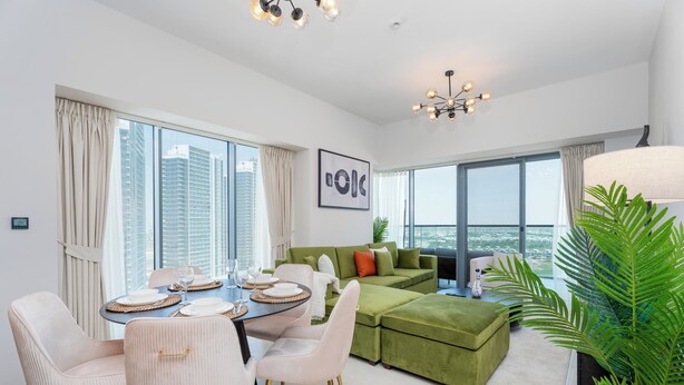 Ein modernes Wohnzimmer mit einem grünen Sofa, einem Esstisch mit Stühlen und einem großen Fenster mit Blick auf die Stadt.
