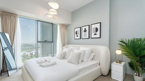 Ein modernes Schlafzimmer mit einem großen Bett, einem Nachttisch mit Lampe, einem Blumentopf und Blick auf die Stadt.