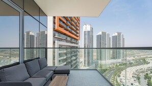Ein Balkon mit einer Couch und einem Tisch, der Blick auf Hochhäuser und die Skyline bietet.