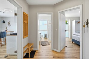 A modern interior with a wooden bench, a bed, and a bathroom visible through an open door. - Carina vacation apartment in Norddeich with balcony and WLAN for up to 4 people (Norddeich)
