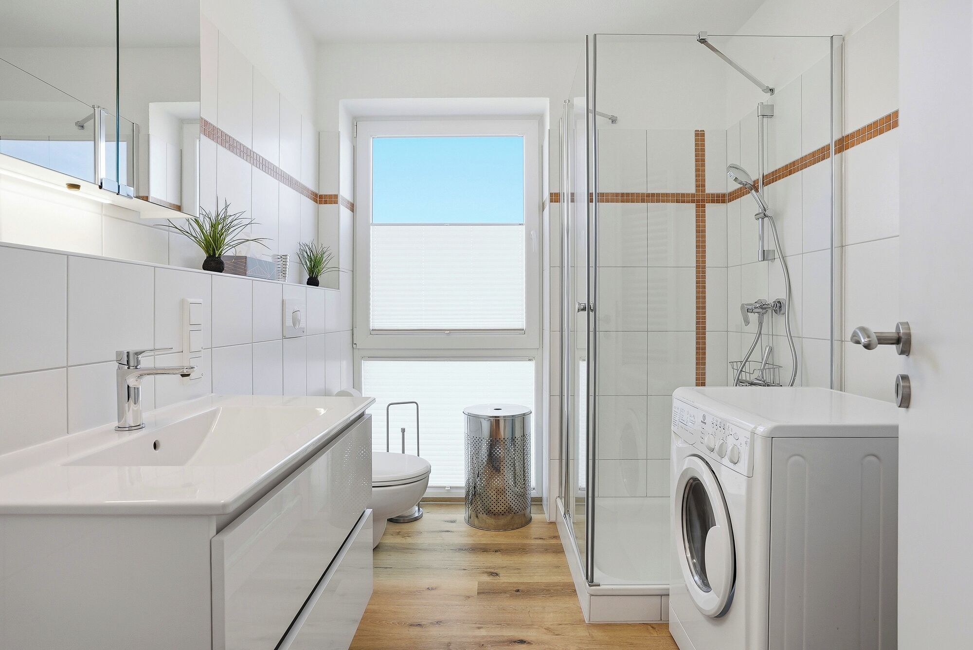 A modern bathroom with a shower, toilet, and washing machine.