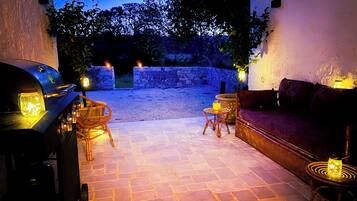 Patio esterno con barbecue, mobili in vimini, divano e illuminazione d'atmosfera.
