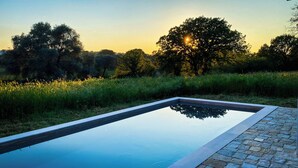 A rectangular swimming pool with a stone border, surrounded by lush greenery and trees, reflecting the sky. - Luxury private condo for 2 w/pool in Apulian hills. Only 15 mins from beach! (Puglia)