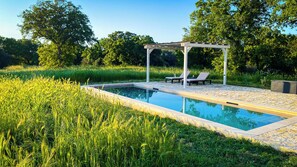 Une piscine rectangulaire agrémentée d’une pergola et de chaises longues, le tout situé dans un espace verdoyant.