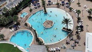 Un'ampia piscina all'aperto con diverse sezioni, circondata da lettini e palme.