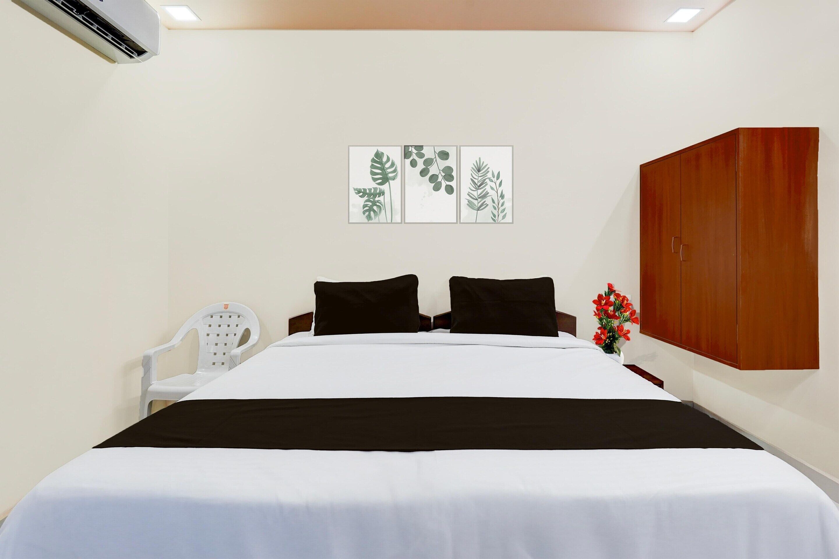 A neatly made bed with a black and white bedspread, a white chair, and a wooden wardrobe.