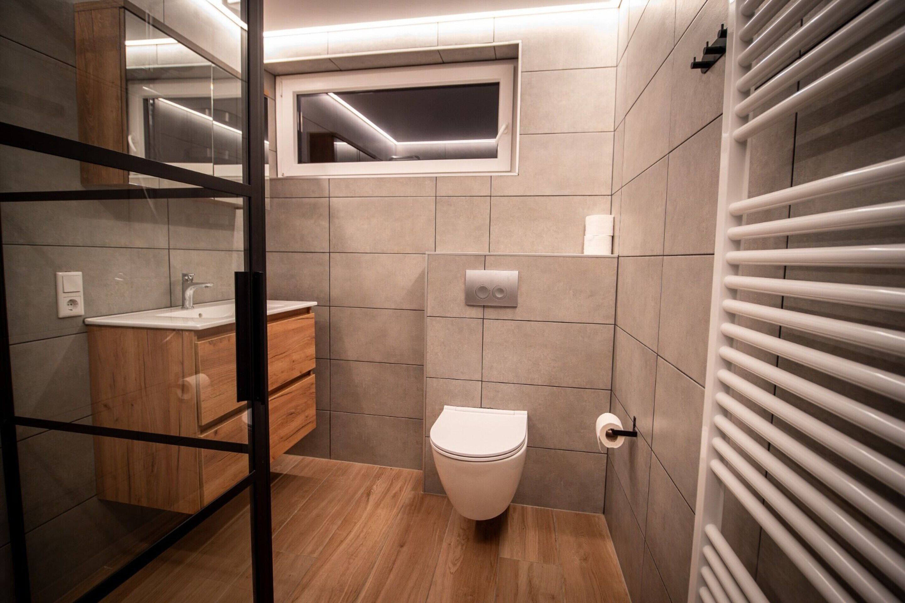 A modern bathroom with a wooden vanity, a toilet, and a glass shower enclosure.