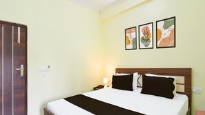 Camera d'albergo con un letto, un comodino, una lampada e una porta. In parete, tre quadri incorniciati.