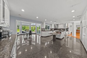 A modern kitchen with a large island, white cabinetry, and a view of a garden. - Private 1-Acre 6BR Luxury Estate - FIFA World Cup 20min to MetLife Stadium & NYC (Cresskill)
