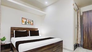 A modern bedroom with a wooden headboard, a bed with white and brown bedding, a small bedside table with a plant, and a wall-mounted artwork.